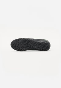 Black athletic shoe sole with textured rubber for grip, featuring a wave pattern and green accents along the edge.