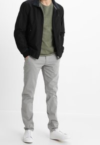 Black bomber jacket with a navy collar, olive green crewneck shirt, light gray slim-fit pants, and white sneakers. Casual outfit.