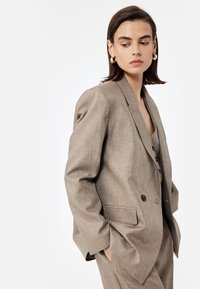 Lichtbruine blazer met een gestructureerde afwerking, enkelvoudige knopen en een geknipte kraag, gecombineerd met een bijpassend topje. Strakke silhouet.