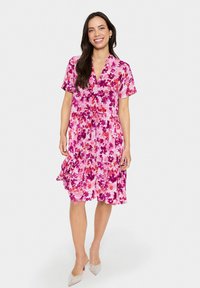 Rochie cu mânecă scurtă, roz, cu un model floral, având decolteu în V, talie strânsă și fustă evazată, de lungime până la genunchi. Finisaj din țesătură texturată.