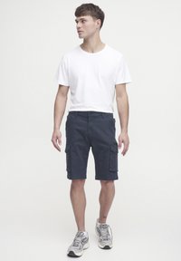 Marinefarbene Cargo-Shorts mit mehreren Seitentaschen, kombiniert mit einem schlichten weißen T-Shirt und grauen Sneakers. Klassisches Design mit geradem Schnitt.