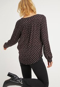 Blouse noire à manches longues, ornée d'un motif floral rose. Tissu léger avec une texture douce et une coupe décontractée, détail d'ourlet incurvé.