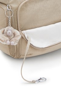 Beige fabric bag with a textured pattern, white panel, zipper closure, and a plush monkey keychain attached to a silver keyring.
