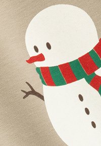 Snemand illustration på beige stof, med en hvid krop, sorte øjne, rød næb og et stribet grønt og rødt tørklæde.
