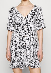 Vestido de manga corta y escote en V en tejido ligero, con un fondo blanco adornado con patrones de corazones negros y detalle de botones en el frente.