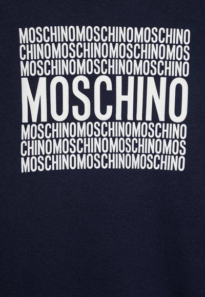 Tumši zila auduma virsma ar atkārtotu balto tekstu "MOSCHINO" dažādās izmēros, radot rakstainu efektu uz materiāla.