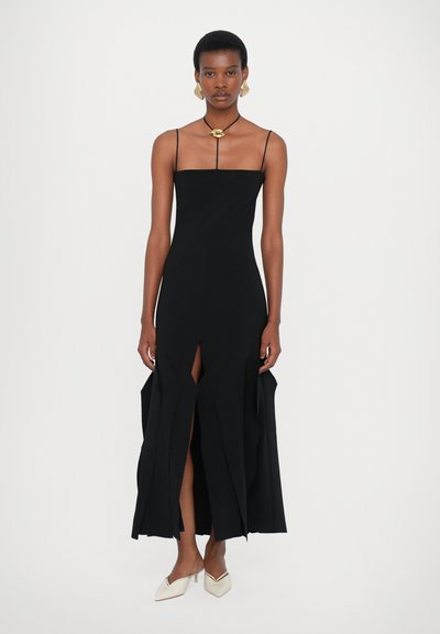 Μαύρο αμάνικο φόρεμα με στενή εφαρμογή και ασύμμετρο φαρδύ στρίφωμα, με μπροστινές σχισμές και απαλό υλικό. Γυναικεία σιλουέτα.