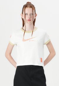 White crop top with olive trim, features orange Nike Air logo and checkered design, made from soft cotton material.