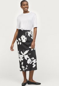 Jupe midi noire à motifs floraux blancs, associée à un t-shirt blanc ample et des chaussures plates noires. Tissu doux, design décontracté.