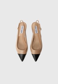 Talons slingback beiges avec un capuchon pointu noir, fabriqués dans un matériau lisse. Comprend une bride arrière et un détail de boucle dorée.