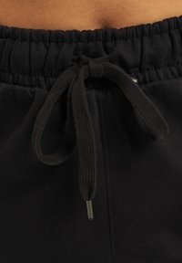 Black jogger pants with an elastic waistband and drawstring closure, featuring a smooth texture and metallic aglet detail on the drawstring.