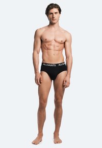 Black cotton brief with elastic waistband featuring "ALLSAINTS" logo. Simple design and form-fitting shape, smooth texture.