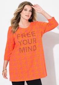 Långärmad tunika i klar rosa med ett orange leopardmönster. Har texten "FRIGÖR DIN SINNE" i svarta rhinestones. Sidoflik detalj vid fållen.