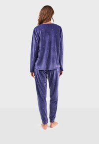 Ensemble de pyjama en velours de couleur violet profond, comprenant un haut à manches longues au fit décontracté et un pantalon assorti. De petites embellissements dispersés apportent une touche de détail.