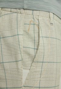 Beige och ljusblå rutig byxa i texturerat tyg med sidofickor och synliga tråddetaljer.