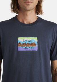 Navyblauwe katoenen t-shirt met een kleurrijk rechthoekig grafisch label waarop de tekst "Element Skateboard Co Worldwide" in verschillende kleuren staat.