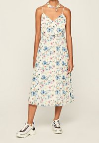 Kwiatowa sukienka midi z cienkimi ramiączkami, z białym tłem, różowym i niebieskim wzorem kwiatowym oraz plecionym pasem w talii. Połączona z masywnymi sneakerami.