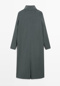 Cappotto lungo di un verde scuro, con colletto alto, taglio dritto e maniche lunghe. Presenta uno spacco centrale sul retro per facilitare i movimenti.
