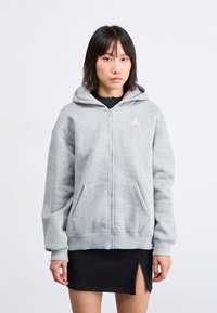 Szürke, cipzáros kapucnis pulóver, kenguruzsebes, ribbelt ujjak. A bal mellrészen fehér Jumpman logó található. Puha, texturált anyag.