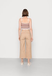 Top cropped às riscas em castanho, branco e pêssego com alças ajustáveis; combinado com calças largas beiges e sapatos de cor clara.