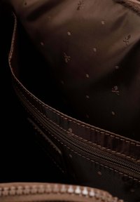 Interior de una bolsa de tela marrón con un sutil patrón de puntos y un bolsillo con cremallera. La textura interior parece suave con detalles de costura reforzada.