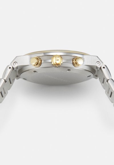 Silver metal watch with a brushed texture, featuring a round case, gold accents on the crown, and two gold pushers on the side.