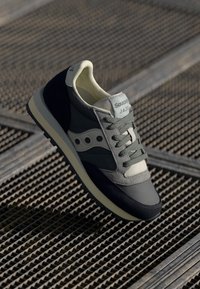 Sneaker grigio e blu navy con una tomaia testurizzata, pannelli a contrasto e una suola intermedia bianca. Presenta lacci verdi e occhioletti esagonali.