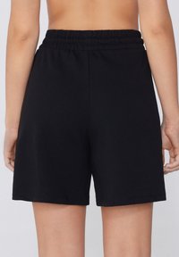 Zwarte sportieve shorts met een elastische tailleband, met een eenvoudig ontwerp en een gladde textuur, die halverwege de dij eindigen voor een ontspannen fit.