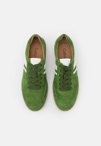 Baskets en daim vert avec des accents en cuir blanc, comprenant des lacets verts et deux bandes blanches le long des côtés. Design athlétique classique.