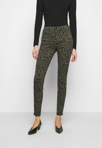 Pantalones de leopardo en verde oliva, con un ajuste slim, cintura media y textura suave. Combinados con zapatos de tacón alto negros.