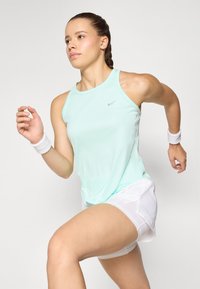 Svijetlo mint zelena atletska majica bez rukava s okruglim izrezom, u kombinaciji s bijelim šortsevima i narukvicama. Sadrži diskretni Nike logotip.