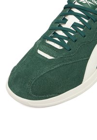 Zielony zamszowy sneaker z białymi akcentami, zaokrąglonym noskiem i sznurowanym designem. Charakteryzuje się teksturowaną powierzchnią i kontrastującymi przeszyciami.