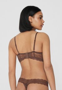 Sujetador de encaje marrón y tanga a juego, con tirantes ajustables, un diseño texturizado y bordes festoneados en ambas piezas.