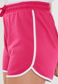 Roze sportieve shorts met een drawstring tailleband, witte zijpiping en geschulpte zoom. Gemaakt van zacht, rekbaar katoenmateriaal.
