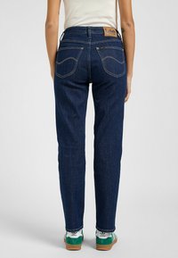 Jeans de mezclilla azul oscuro con corte recto, que presentan detalles de costura y dos bolsillos traseros. Etiqueta de la marca Lee visible en la cinturilla.