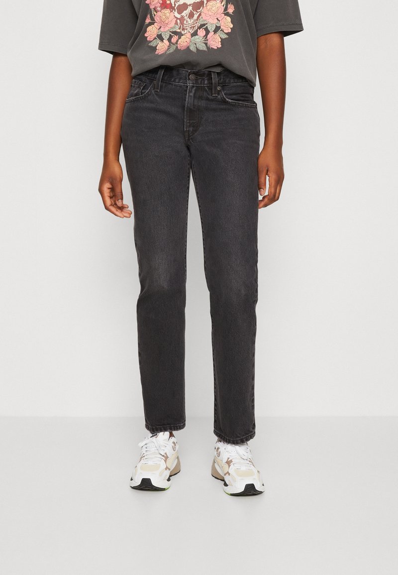 Jeans de mezclilla negra con corte recto, diseño clásico de cinco bolsillos y un ligero desgaste. Combinados con una camiseta gráfica y zapatillas.
