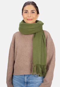 Écharpe vert olive en tissu doux, avec des extrémités à franges, portée sur un pull marron clair. Design simple, sans motifs ni éléments métalliques visibles.