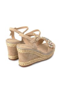 Sandales compensées beiges avec une surface en suède texturé, dotées d'une sangle décorative en perles et d'un détail en jute tissé sur le talon.