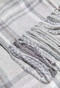Écharpe à carreaux dans des tons de gris, fabriquée à partir d'un tissu doux, dotée de franges aux extrémités, avec une surface texturée et un motif subtil.
