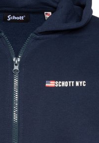 Felpa con zip di colore blu navy realizzata in tessuto a coste. Presenta una zip frontale, un logo con la bandiera degli Stati Uniti e una texture morbida.