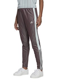 Pantalons de sport bordeaux à rayures avec des panneaux latéraux bleu clair. Taille élastique et jambes fuselées. Logo Adidas sur la cuisse. Associés à des baskets blanches.