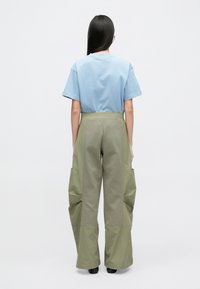 Γαλάζια μπλούζα με στρογγυλή λαιμόκοψη, συνδυασμένη με ψηλόμεσα, φαρδιά παντελόνια σε ελιά πράσινη απόχρωση, με μεγάλα τσέπες και υφή στην επιφάνεια.