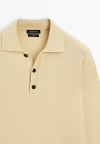 Polo shirt in lana beige con colletto piatto, tre bottoni neri e texture a coste su polsini e orlo. Design minimale.