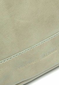 Borsa in pelle verde chiaro con una consistenza liscia, caratterizzata da cuciture visibili e un branding sottile lungo il bordo inferiore.