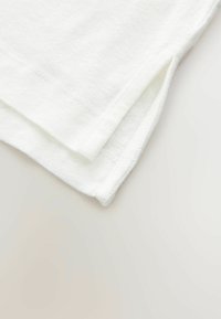 White cotton fabric with a smooth texture, featuring a side split at the hem and clean stitching along the edges.