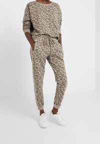 Sudadera de estampado de leopardo en beige y gris, combinada con joggers a juego, que cuentan con una cinturilla elástica y bolsillos laterales. Llevada con zapatillas blancas.