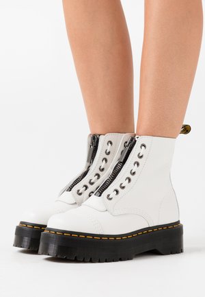 Stivali alla caviglia in pelle bianca con chiusura a zip, suola platform nera con cuciture gialle e occhielli in metallo. Texture liscia.