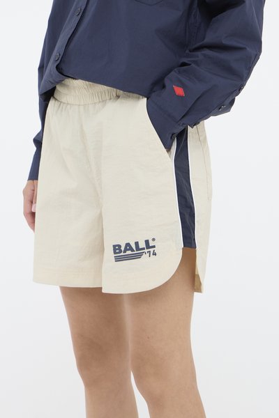 Beige shorts med elastisk midjebånd, marineblå sidepaneler og en trykt «BALL»-logo i blå. Stoffet ser lett ut med en glatt tekstur.