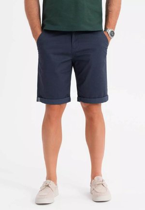 Marineblauwe shorts met omgeslagen randen, gemaakt van een katoenmix, met zijzakken. Gepaard met lichtgekleurde canvas sneakers.