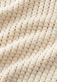 Crèmekleurige gebreide stof met een textuurpatroon van verhoogde steken en open weefsels. Zacht en flexibel, ideaal voor diverse textieltoepassingen.